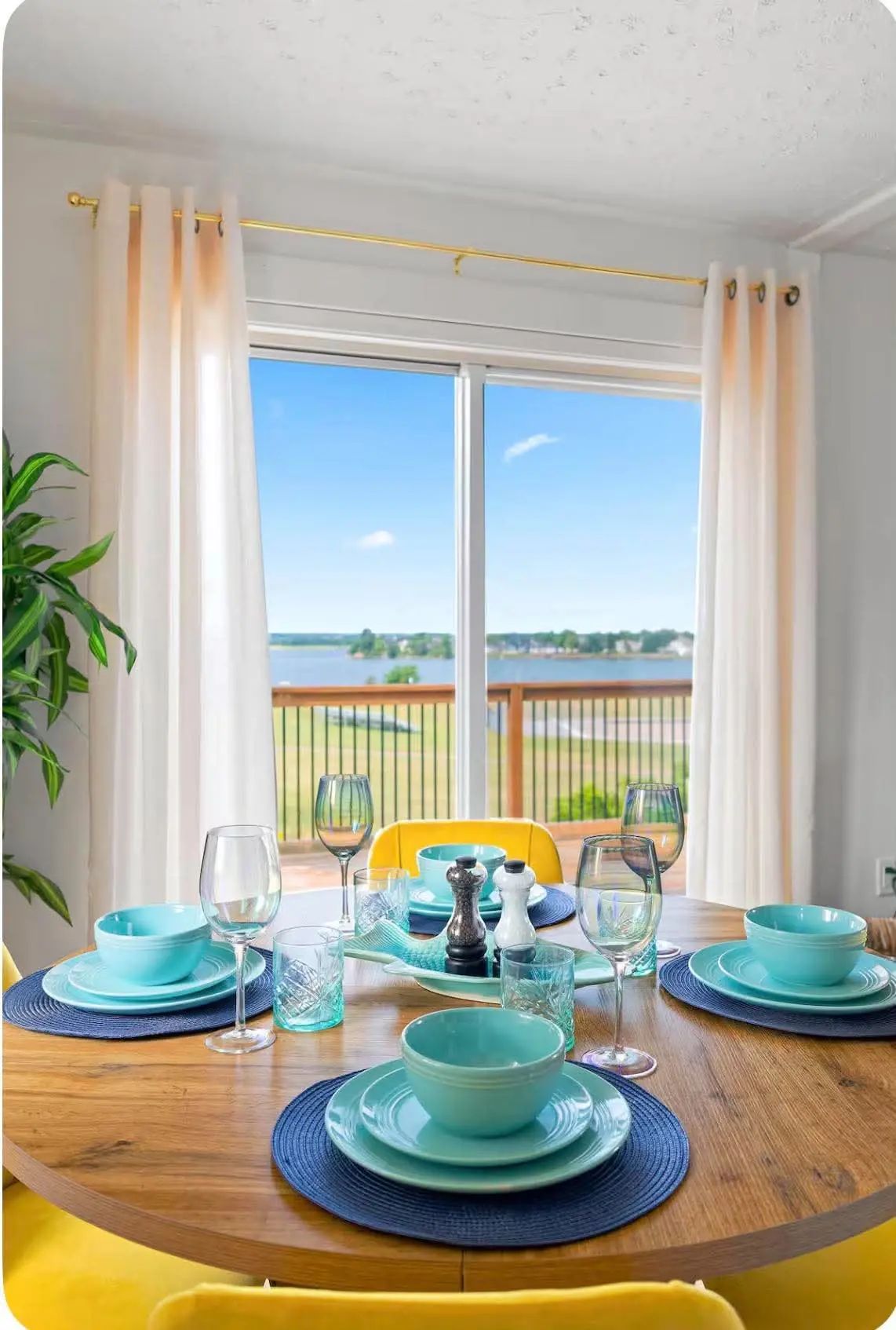 Dining table set with turquoise dishes in front of a window with a water view