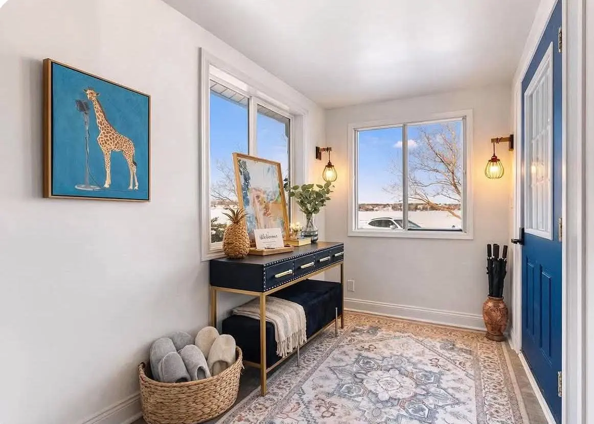 Bright entryway of a rental home with a blue front door, a console table and a basket of guest slippers
